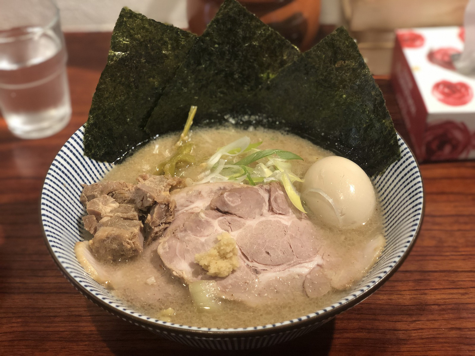 大ぶりのチャーシュー2枚（うち1枚は生姜が乗っている）・角切りチャーシュー・斜め薄切りの白ネギ、山クラゲ、味玉が乗り、縁に3枚の6切り？の海苔が添えられた、白っぽい茶色に濁ったスープの味噌ラーメン。iPhoneのポートフォリオモードで加工されている。
