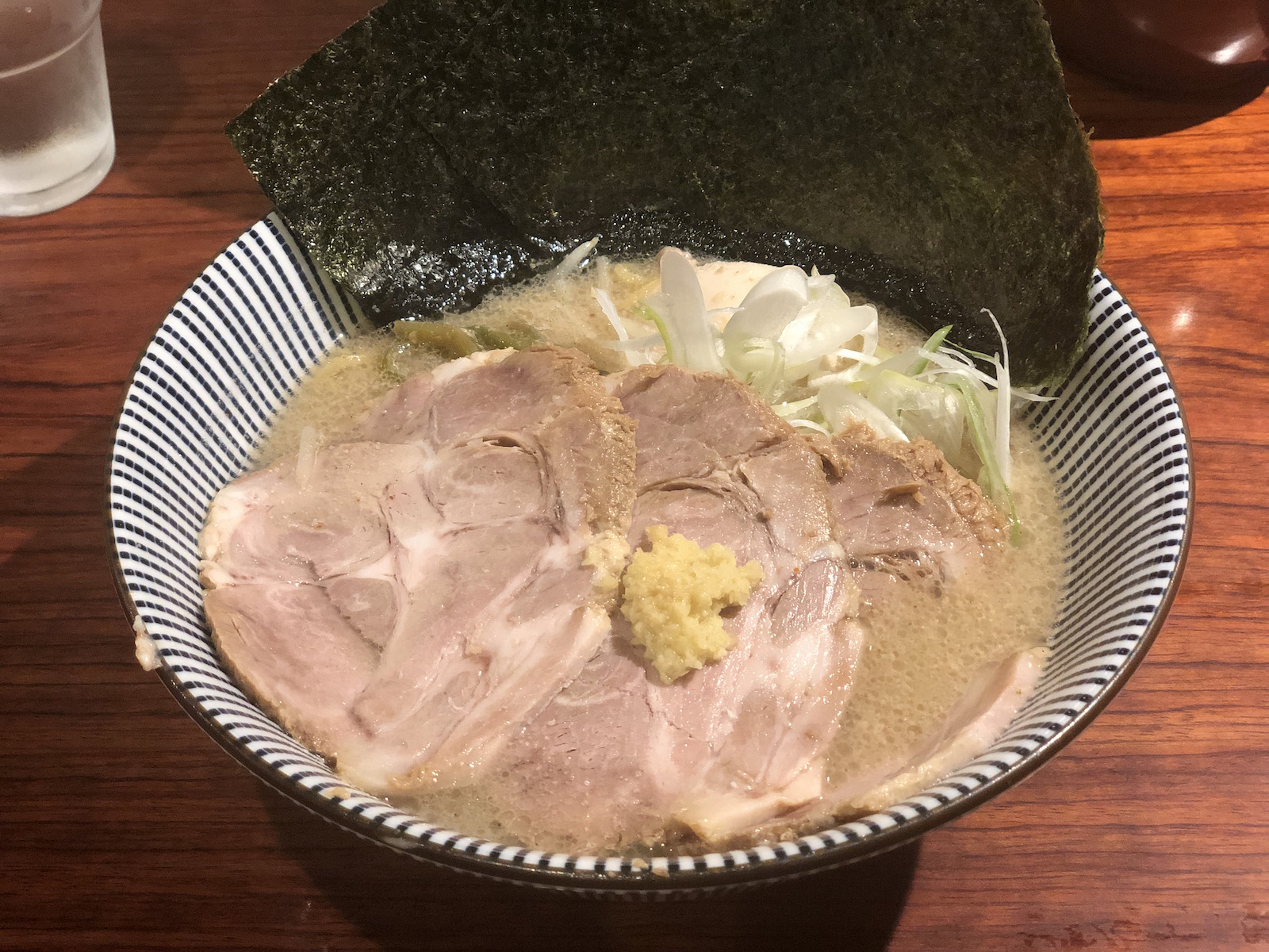 大ぶりのチャーシュー3枚（うち1枚は生姜が乗っている）・斜め薄切りの白ネギ、山クラゲ、味玉が乗り、縁に3枚の6切り？の海苔が添えられた、白っぽい茶色に濁ったスープの味噌ラーメン