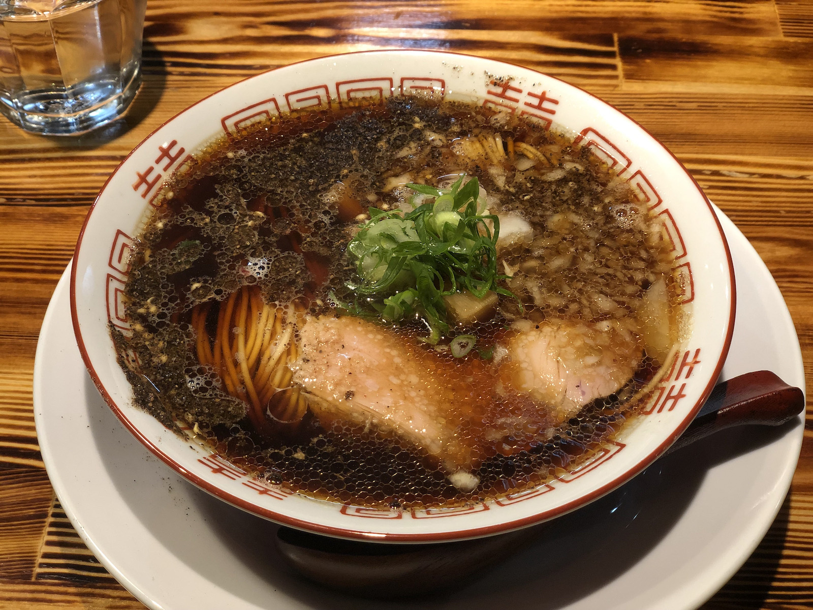 刻んだ玉ねぎと胡椒らしきものが浮かぶ黒に近い茶色のスープに、大ぶりのチャーシュー・太いメンマ・輪切りのネギが乗ったラーメン