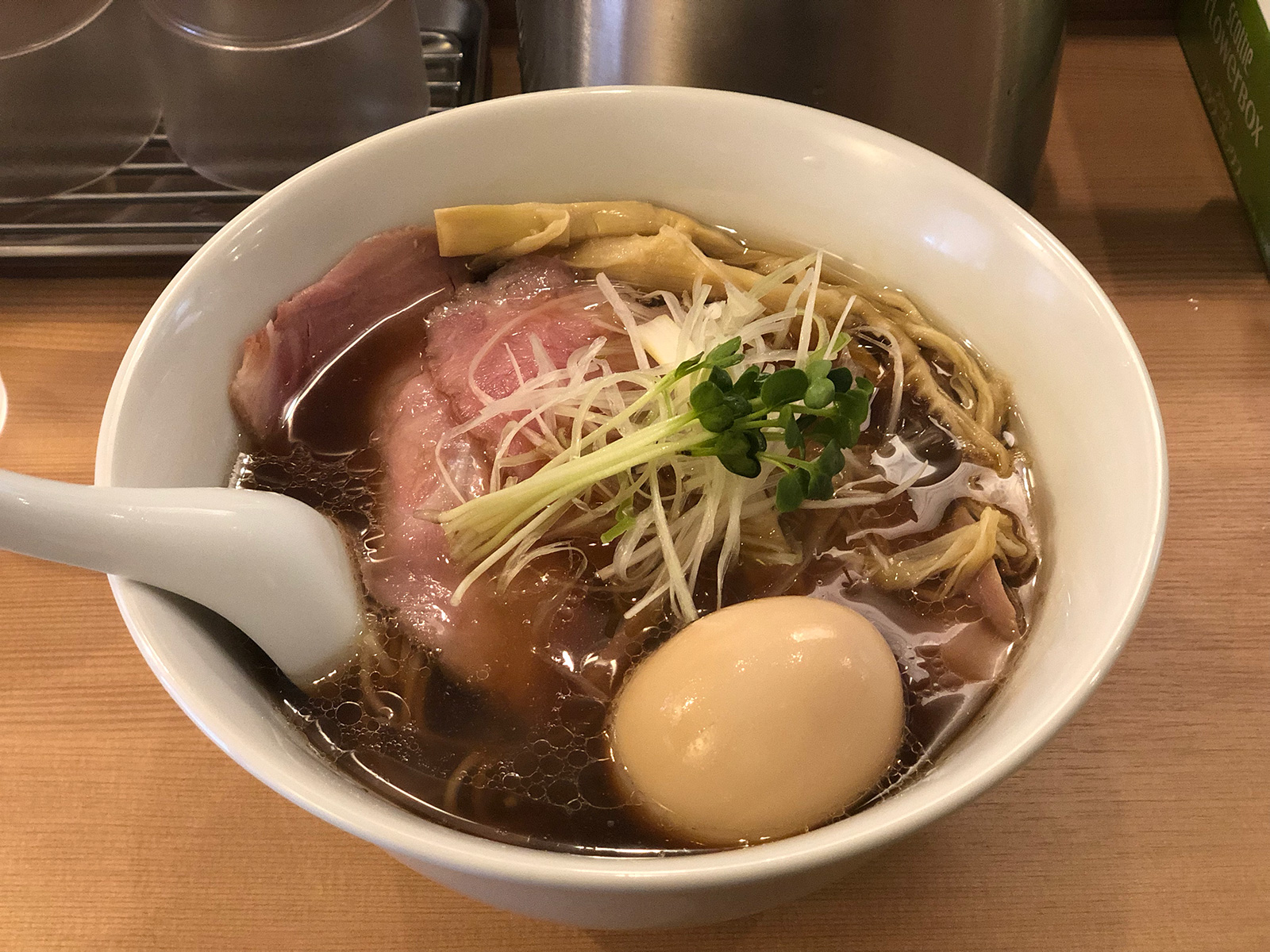 チャーシュー・煮玉子・白髪ネギ・カイワレが乗った、濃い茶色の澄んだスープのラーメン