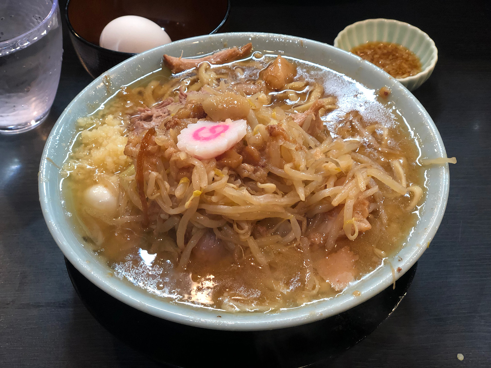 ナルト・シナシナのモヤシ・肉片・ニンニクが乗っている全体的に茶色がかったラーメン